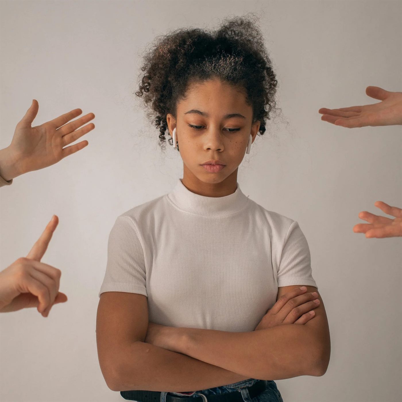 A girl standing with her arms crossed while hands point at her